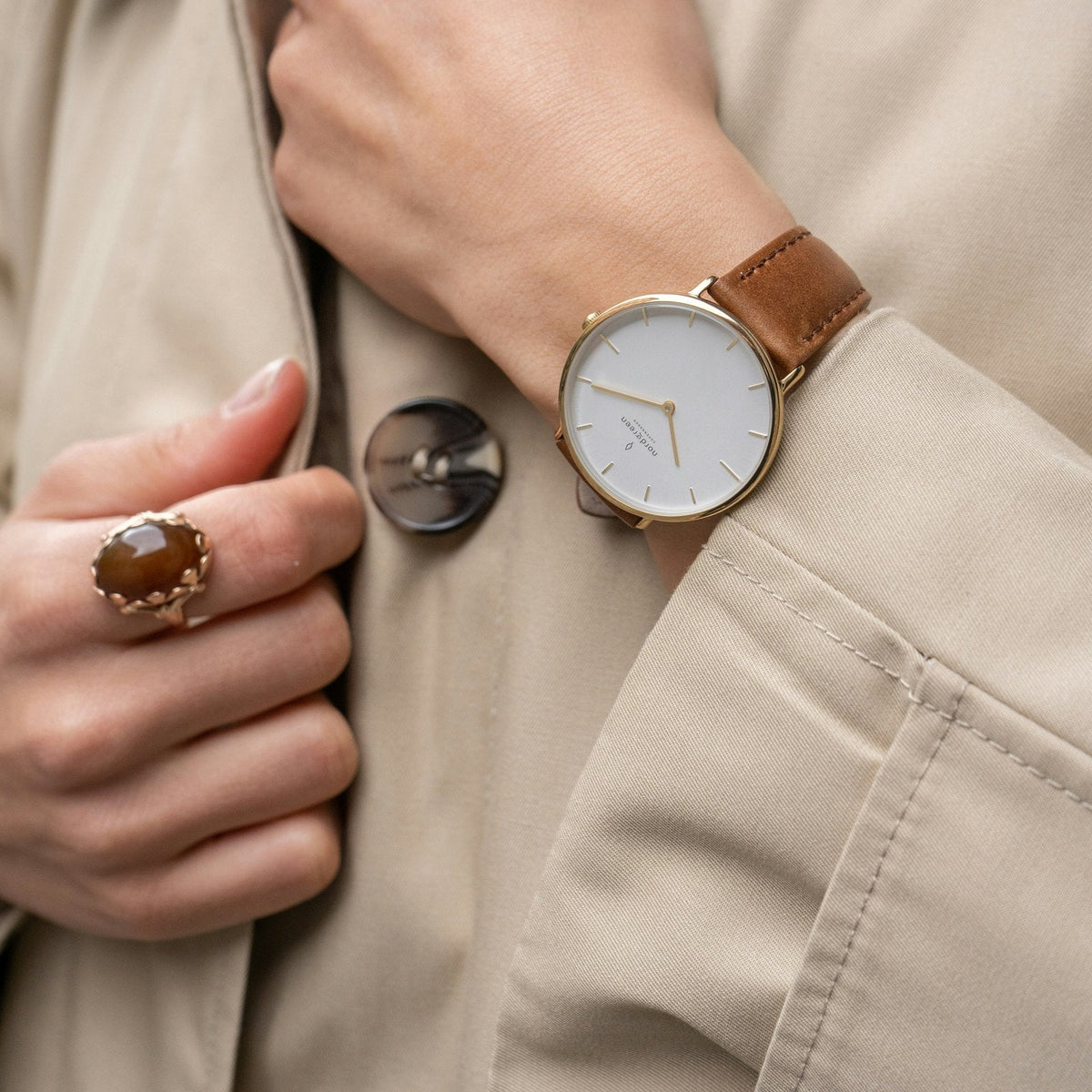 A woman in a trench coat holding the HIYD sensor beside her leather strap watch