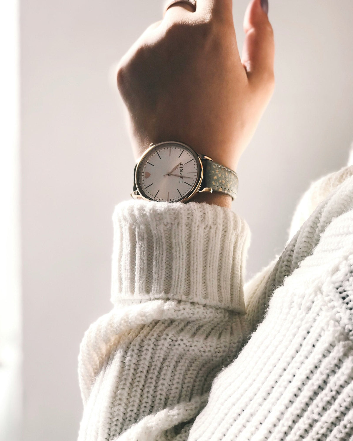 A slim watch worn on a wrist above a cream knit sweater cuff